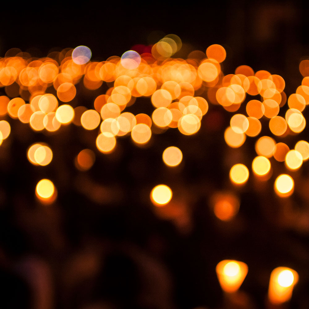 Warm orange bokeh lights in a dark scene, resembling a sea of candles at night fall of glow